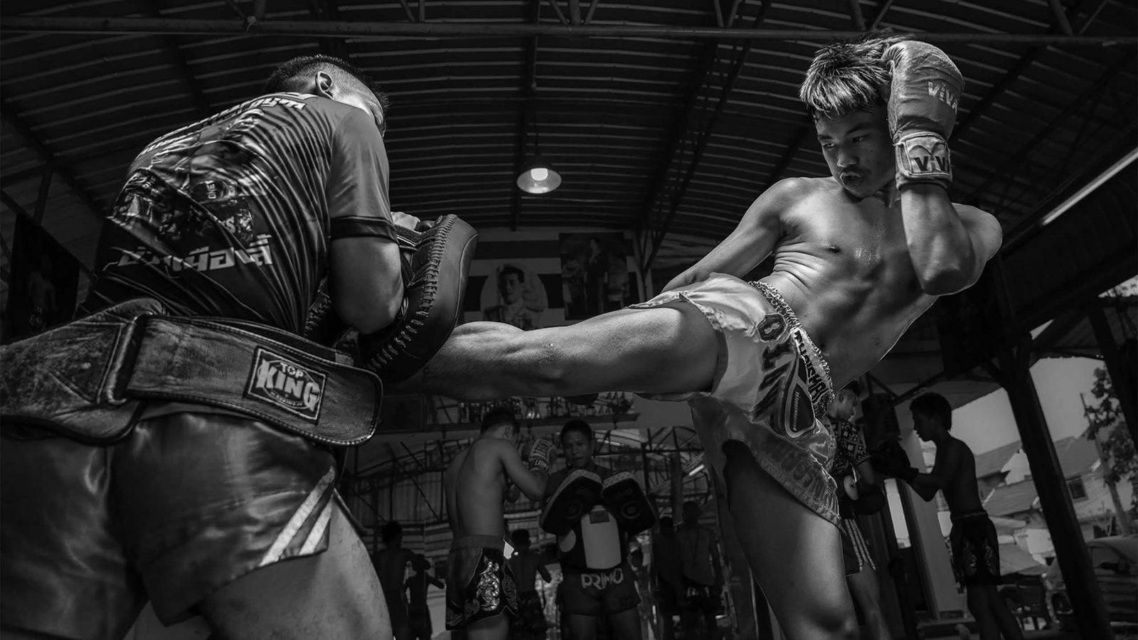 A fighter kicks pads inside Rambong Muay Thai Gym’s covered Chiang Mai training space.
